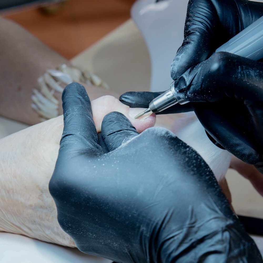 Podóloga con guantes realizando tratamiento de uñas con torno profesional
